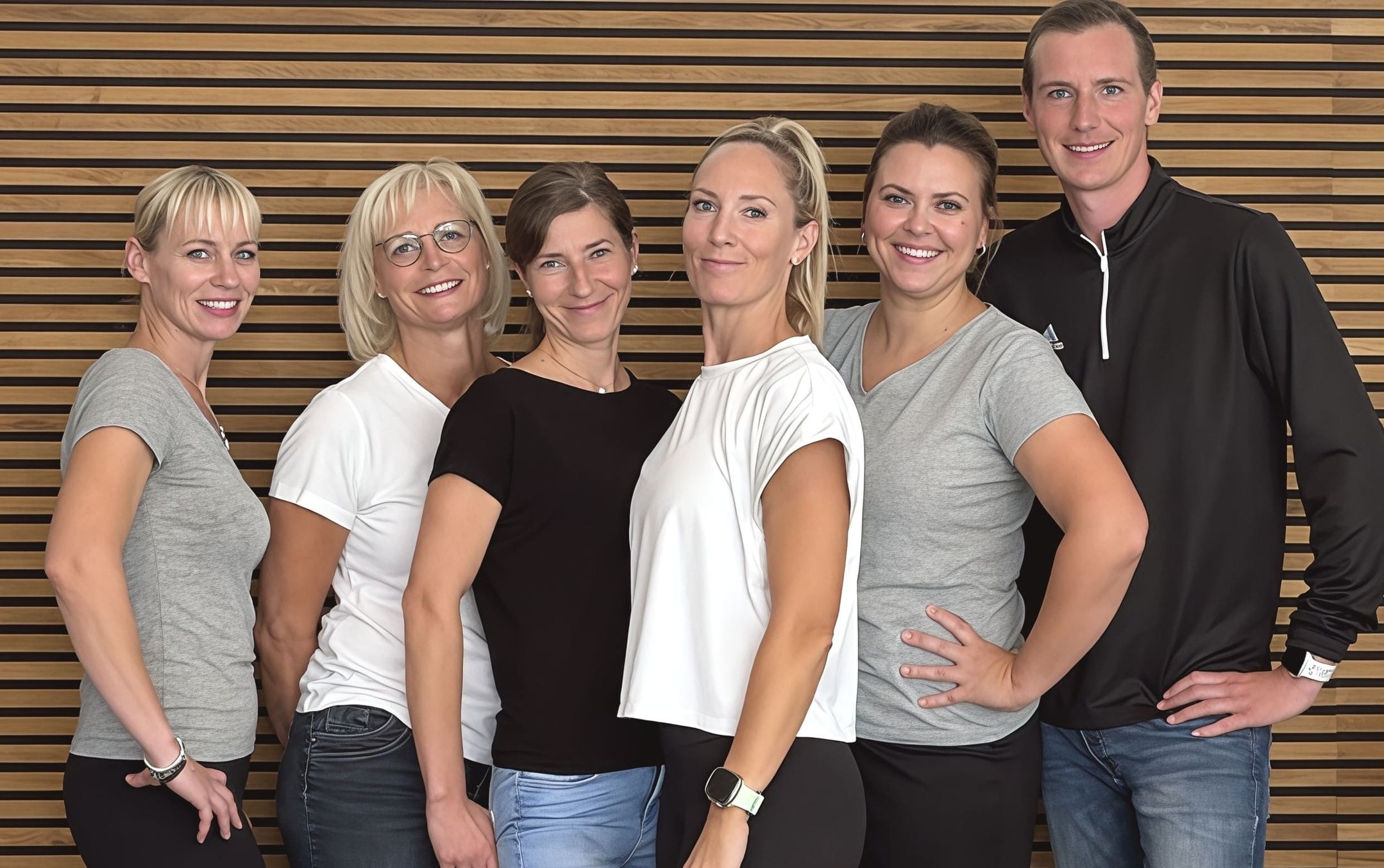 Sechs lächelnde Personen in Adidas-Sportkleidung vor einer Holzwand-Kulisse